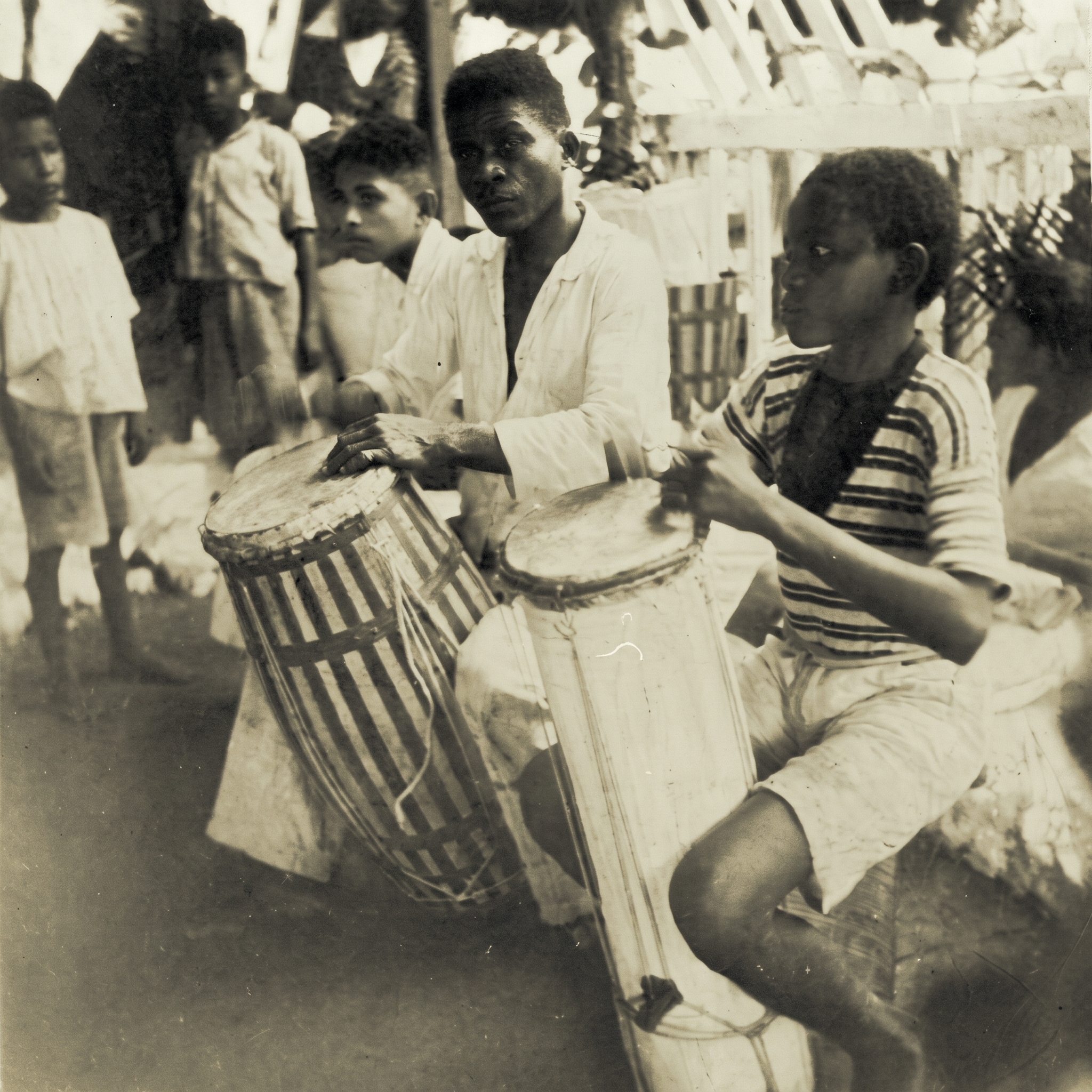 Dois tocadores de tambor num terreiro, em foto antiga em preto e branco
