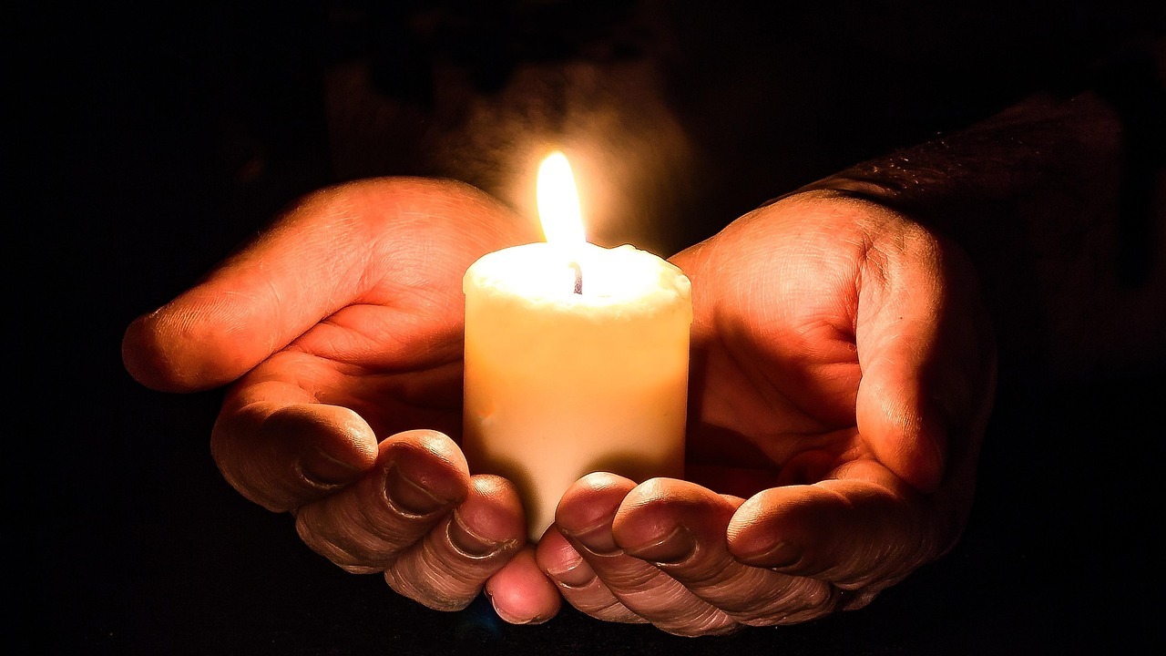 Mãos abertas segurando uma vela acesa